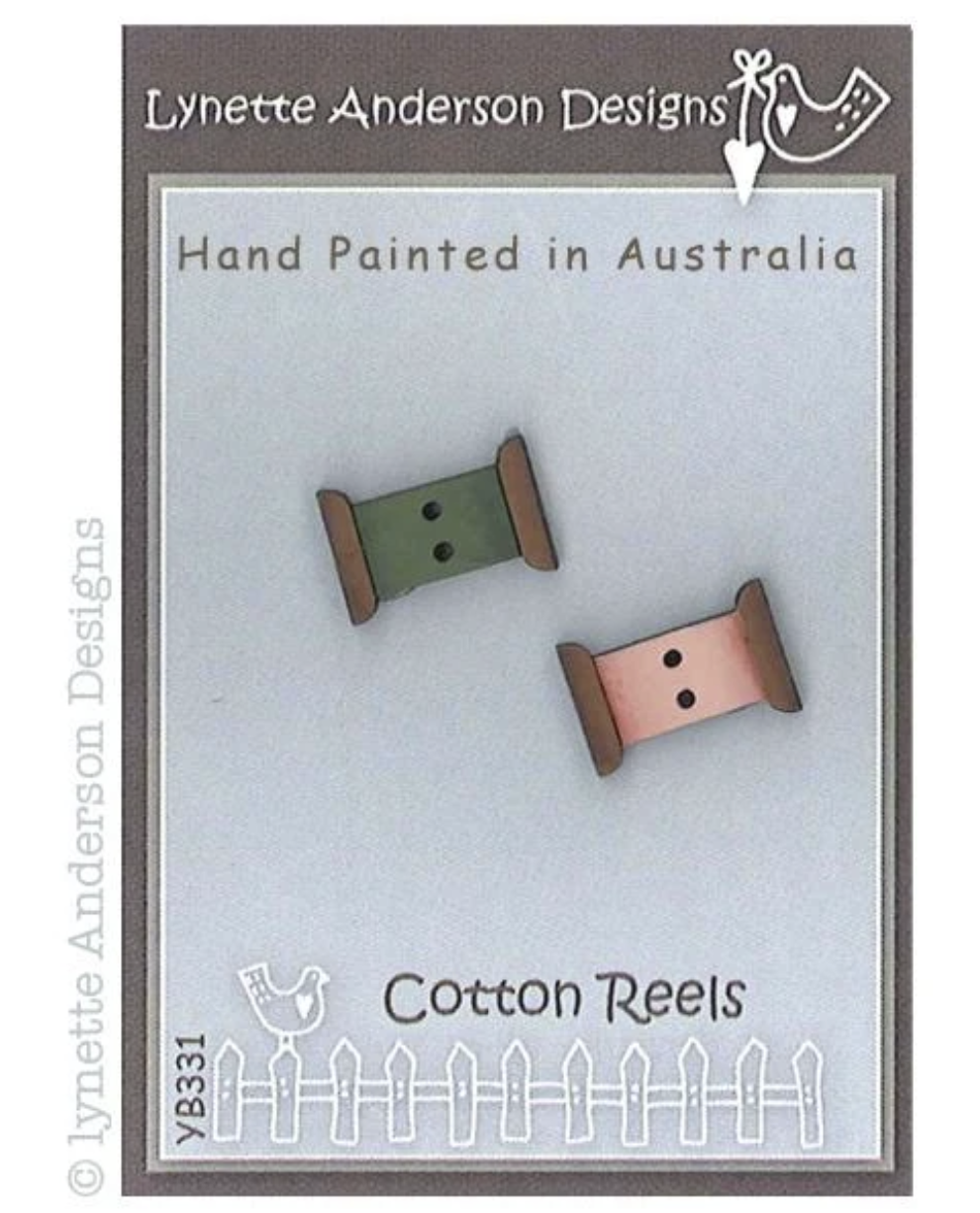 Lynette Anderson Designs 'Cotton Reels' YB331 craft embellishments, featuring two hand-painted cotton reel shapes in olive green and dusty pink on a light blue-gray backing card.