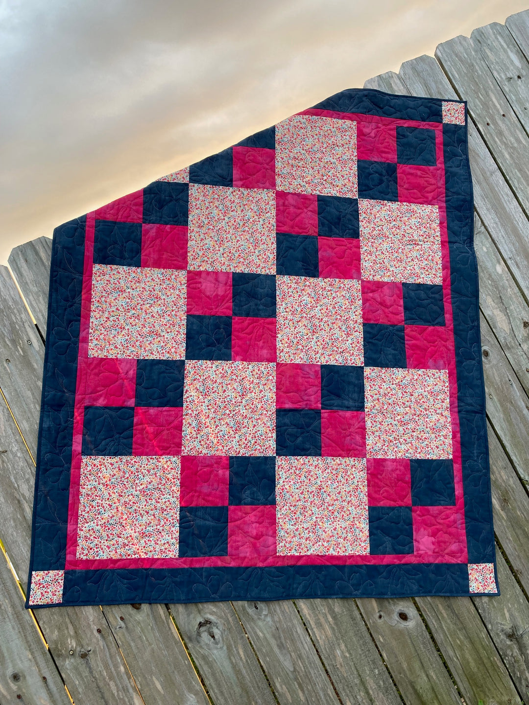 A completed quilt with a checkered pattern of red, navy, and beige squares laid out on a wooden surface.